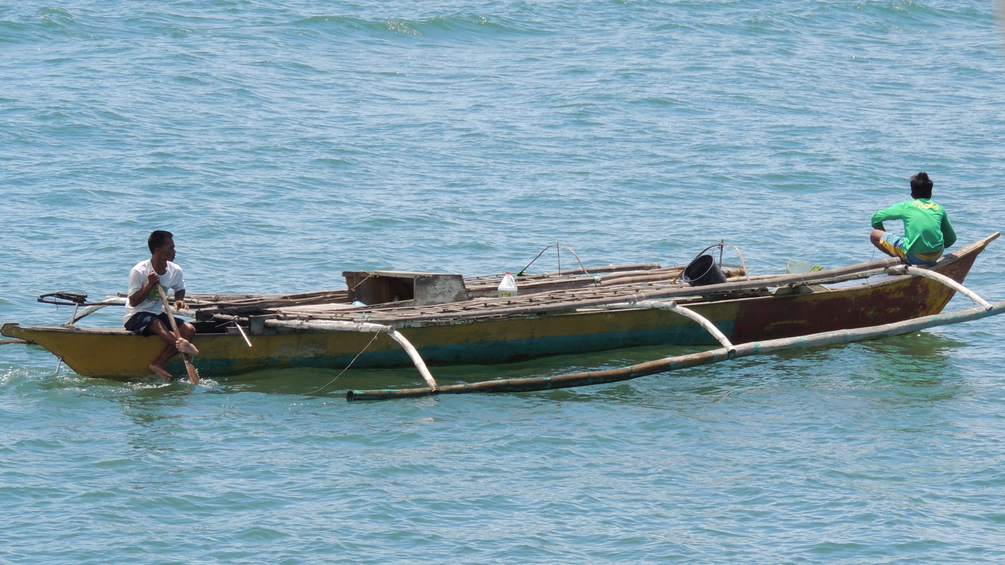 Ein kleines Fischerboot mit zwei Menschen drauf im Meer.