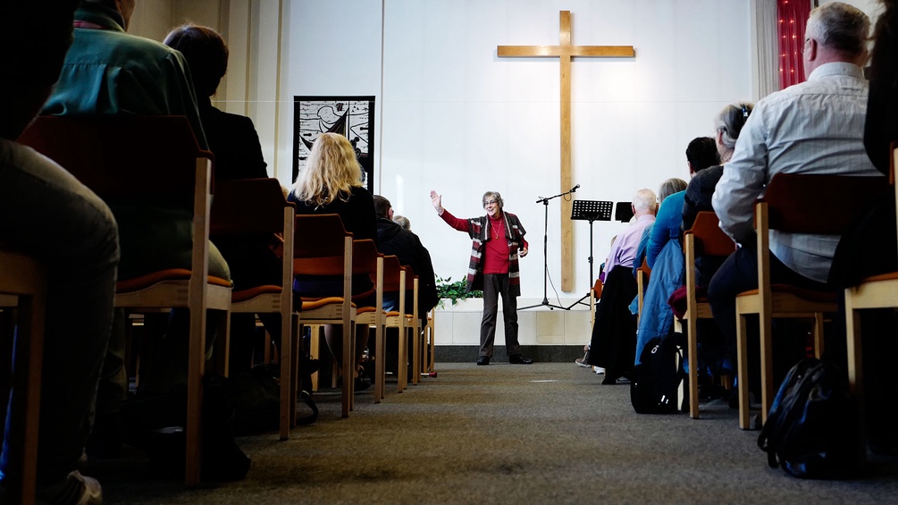 Evangelische Freikirche, Frau steht vor Kreuz und spricht