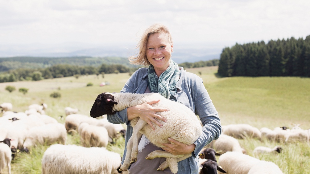 Frau auf einer Alm hält Schaf im Arm 