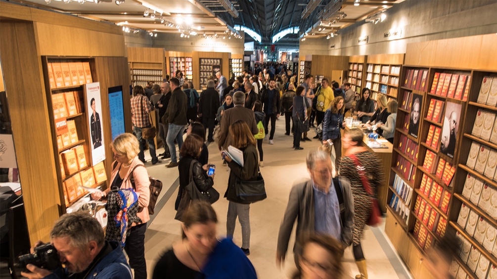 Ein Gang auf der Frankfurter Buchmesse: Man sieht viele Menschen, an der Wand Bücherregale