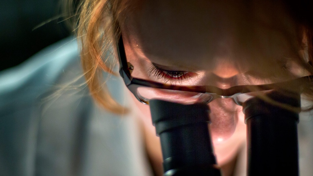 Frau blickt durch Mikroskop