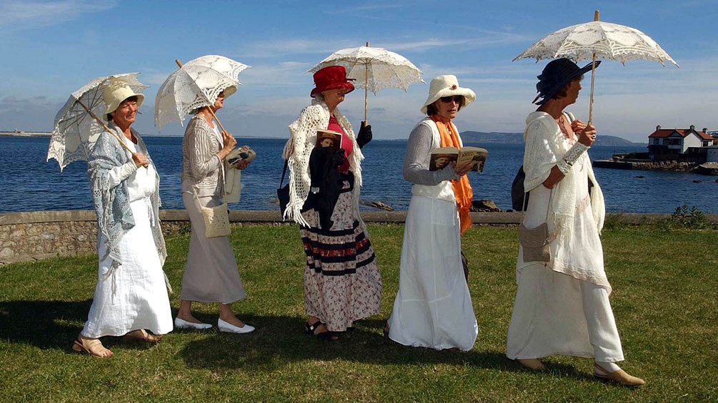 Fünf verkleidete Damen mit Büchern und Sonnenschirmen