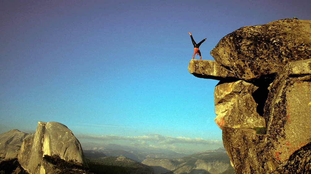 Ein Extremkletterer macht einen Handstand auf einem Felsvorsprung