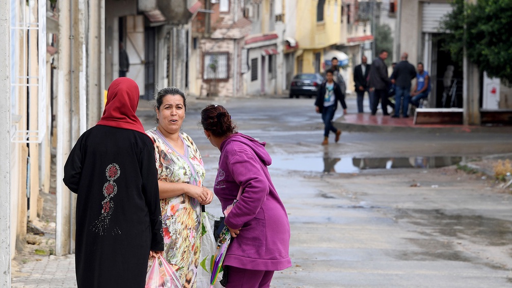 Frauen auf der Straße, im Hintergrund Männer in einer tunesischen Stadt