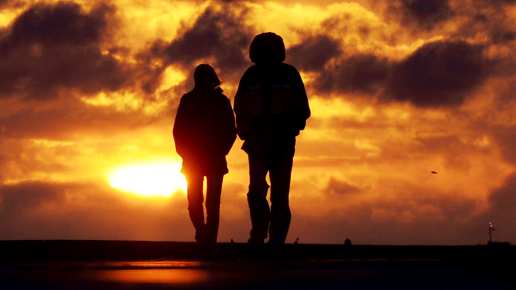 Zwei Menschen spazieren in den Sonnuntergang