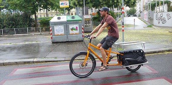 Junger Mann fährt mit Lastenrad auf der Straße
