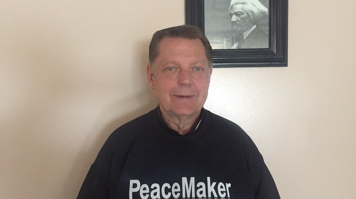 Porträt Father Mike. Er trägt einen Pullover mit der Aufschrift "PeaceMaker".