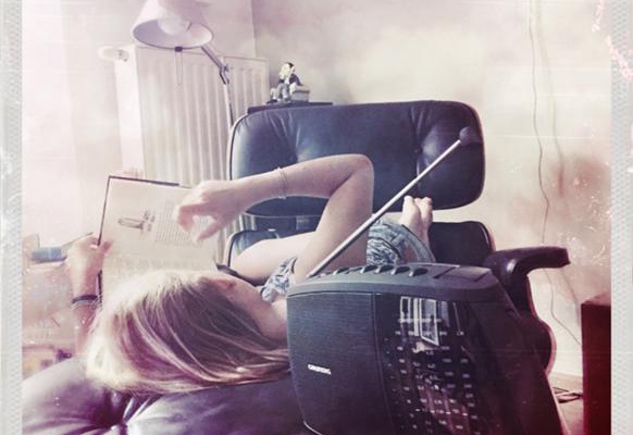 Eine junge frau liegt auf einer Couch, hält ein Buch in der Hand, davor ein Radiogerät.