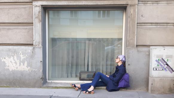 Eine Frau sitzt auf der Straße vor einem großen Fenster. Auf der Fensterbank ein Radiogerät.