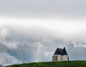 Eine kleine Kapelle steht vor einer frischverschneiten Landschaft