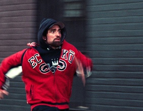 Junger Mann, mit schwarzer Kaputze und roter Jacke, rennt