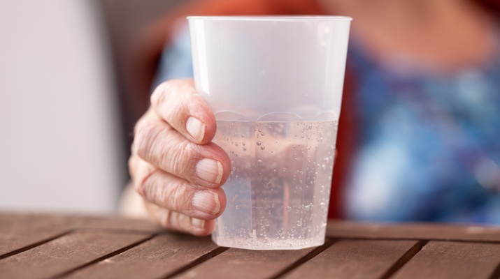 Die Hand einer alten Dame hält einen Plastikbecher mit Mineralwasser, Pflegeheim