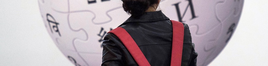 Frau mit Rucksack steht vor Wikipedia-Plakat