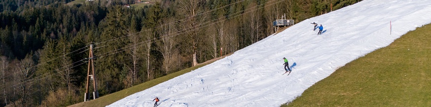 Skipiste mit Kunstschnee, links und rechts Wiese