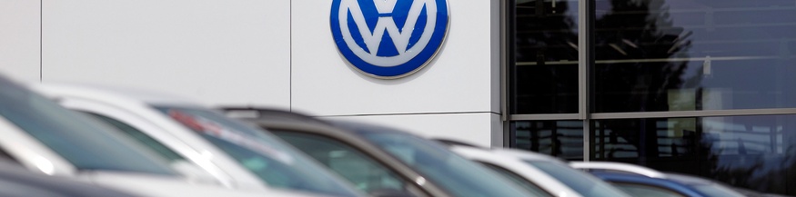 Großes VW-Zeichen bei einem Autohändler, diverse Autos im Vordergrund in Unschärfe