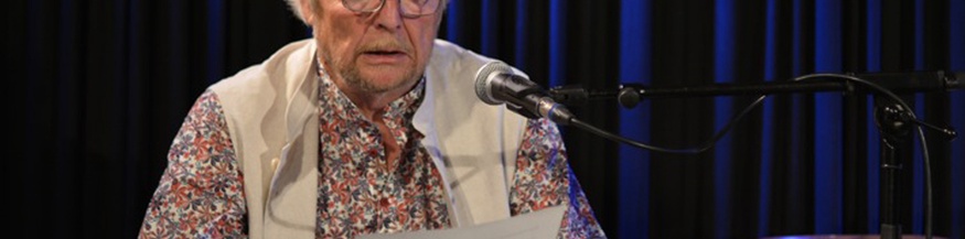 Roland Knie sitzt am Mikrophon und liest vor.