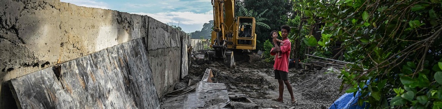 Ein Mann steht mit Kind in Armen neben einem unfertigen Damm in Plaridel in der Bulacan-Region, Philippinen