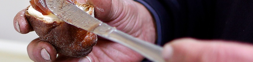 Obdachloser Mann bestreicht sich ein Stück Gebäck