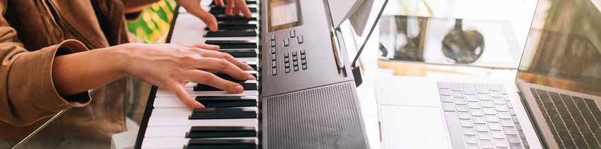 Frau nimmt zuhause am Keyboard Musik auf, Laptop