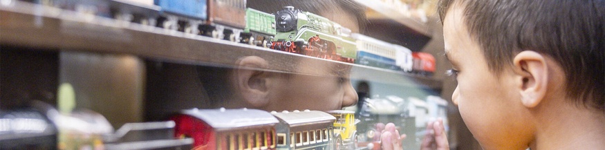 Kind im Spielzeugmuseum betrachtet Modelleisenbahnzüge