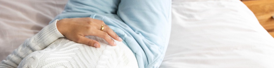 Frau liegt auf dem Bett und hat eine Hand auf dem Bauch