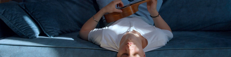 Mann sitzt kopfüber mit Ukulele auf einem Sofa und hat die Augen geschlossen
