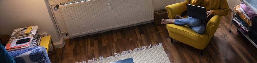 Person sitzt zuhause in einem gelben Armsessel und arbeitet am Laptop