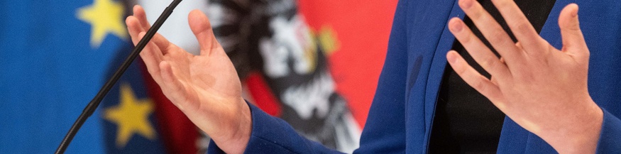 Diskutierende Hände, Mikrofon und Fahnen im Hintergrund
