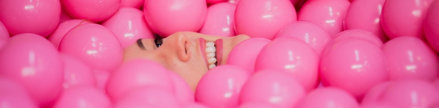 Das Gesicht einer Frau verschwindet in einem pinken Bällebad.