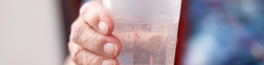 Die Hand einer alten Dame hält einen Plastikbecher mit Mineralwasser, Pflegeheim