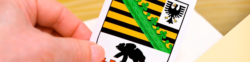Hand wirft Landeswappen des deutschen Bundeslandes Sachsen-Anhalt in eine Wahlbox