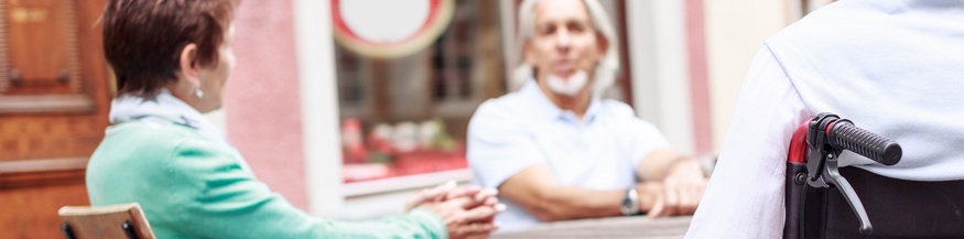 Menschen sitzen vor einem Café, ein Mann sitzt im Rollstuhl