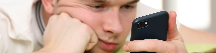 Junger Bursche schaut gelangweilt in ein Smartphone