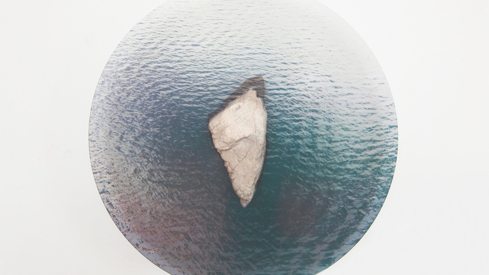 Kunstinstallation mit einem Stein auf einer Glasplatte als Insel