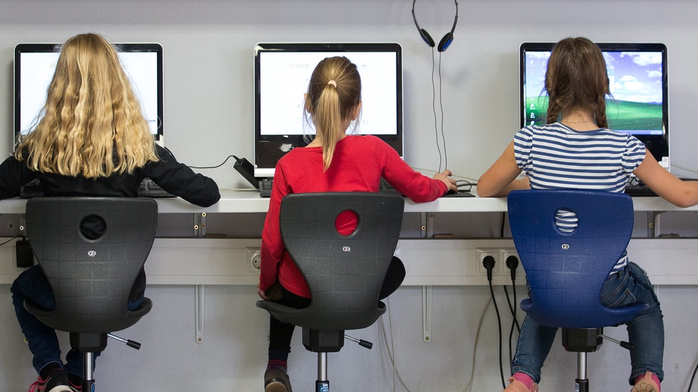 Schülerinnen sitzen in einem Klassenraum einer Grundschule an Computern und arbeiten.