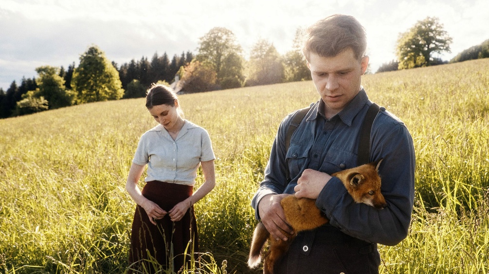 "Der Fuchs", Filmstill: Mann und Frau auf einer Wiese, Mann hält Fuchs in den Armen
