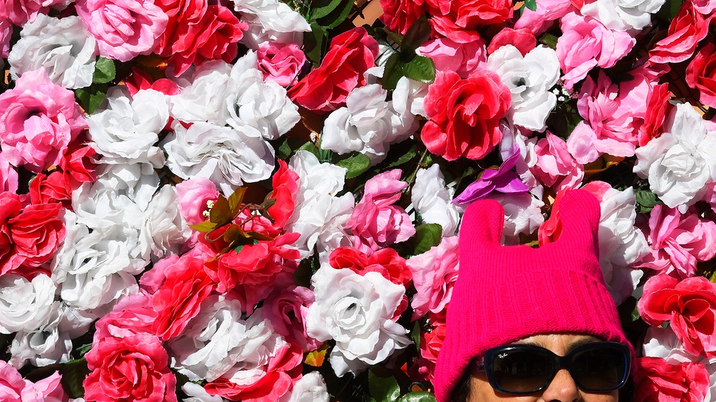 Rosafarbene Rosen und eine Dame, die einen "Pussyhat" trägt mit Sonnenbrille