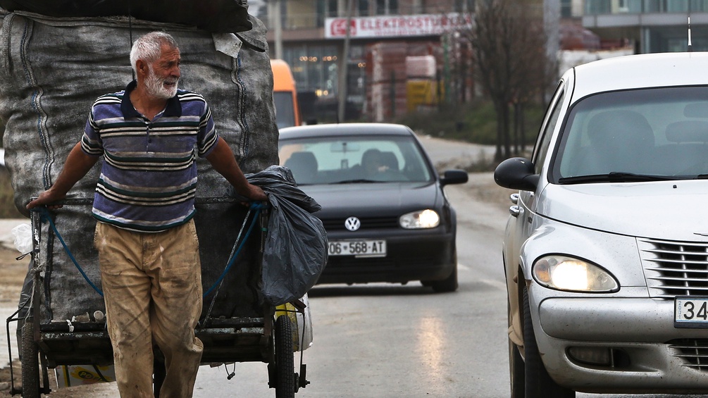 Ein Mann zieht einen Anhänger, daneben Autos im Kosovo