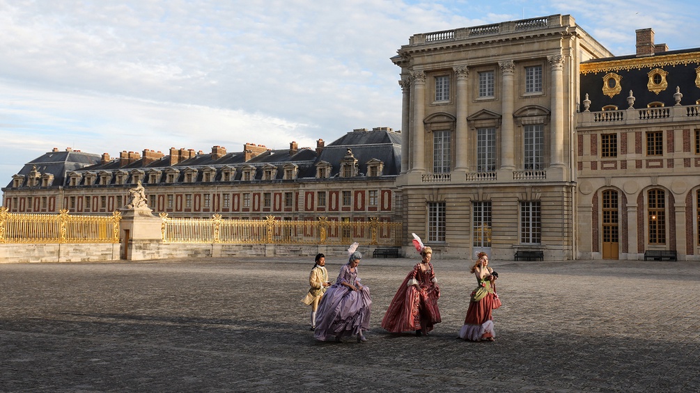 Gäste in barocken Kleidern vor dem Schloss Versailles.