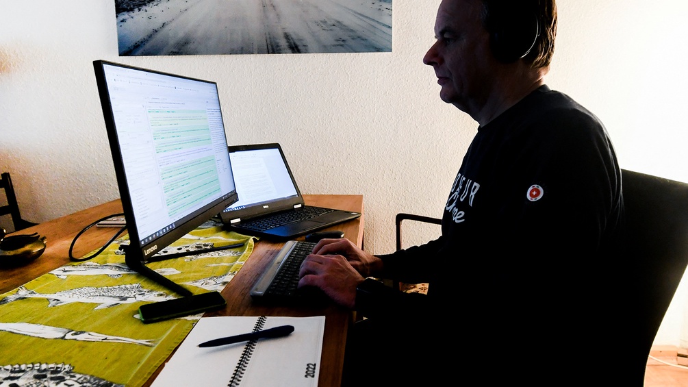 Mann arbeitet an einem Tisch mit Laptop und Monitor, Home Office