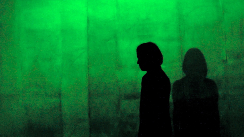 Grüner Hintergrund, davor zwei Frauen im Gegenlicht