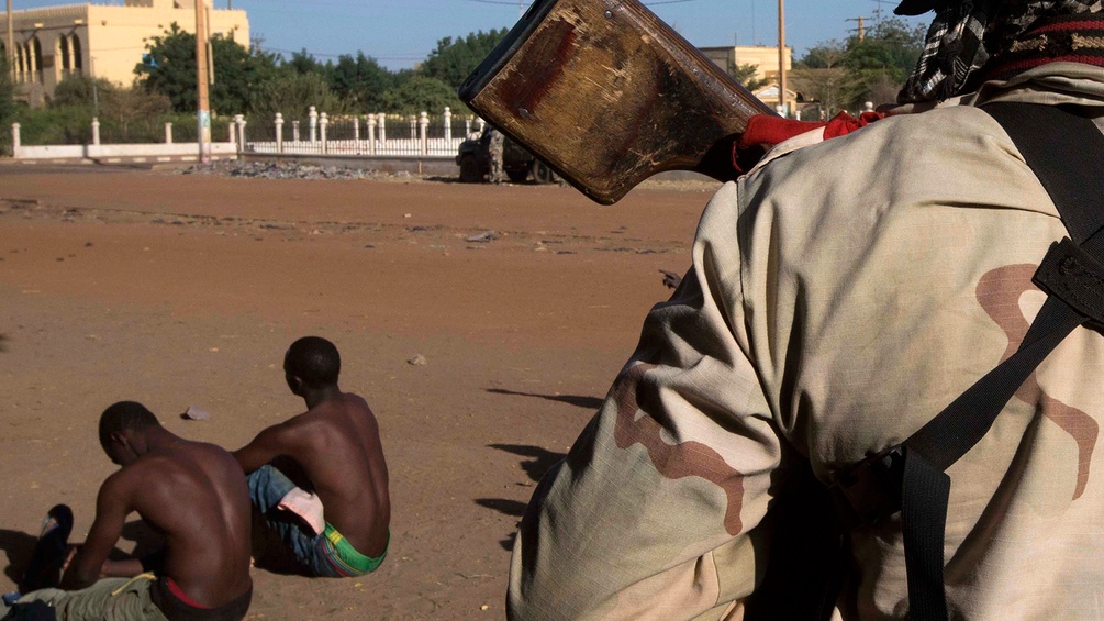 Soldat in Mali vor zwei jungen Männern, die auf dem Boden sitzen