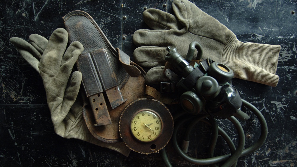Alte Hanschuhe, ein Waffenhalster, eine Gasmaske und eine Uhr.