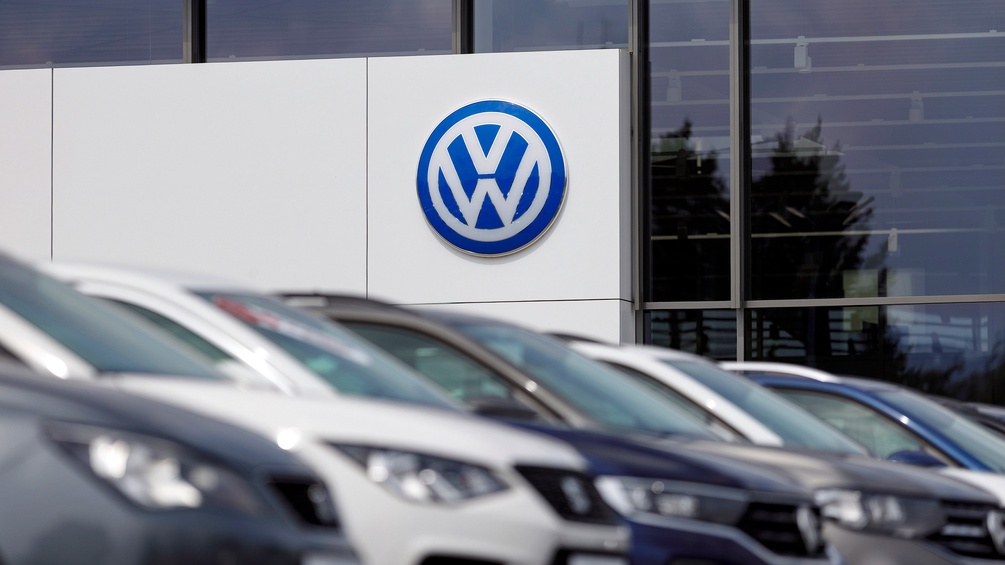 Großes VW-Zeichen bei einem Autohändler, diverse Autos im Vordergrund in Unschärfe