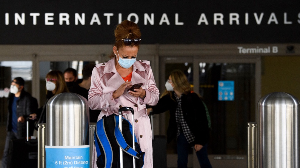 Eine Frau am Flughafen mit Maske und Gepäck.