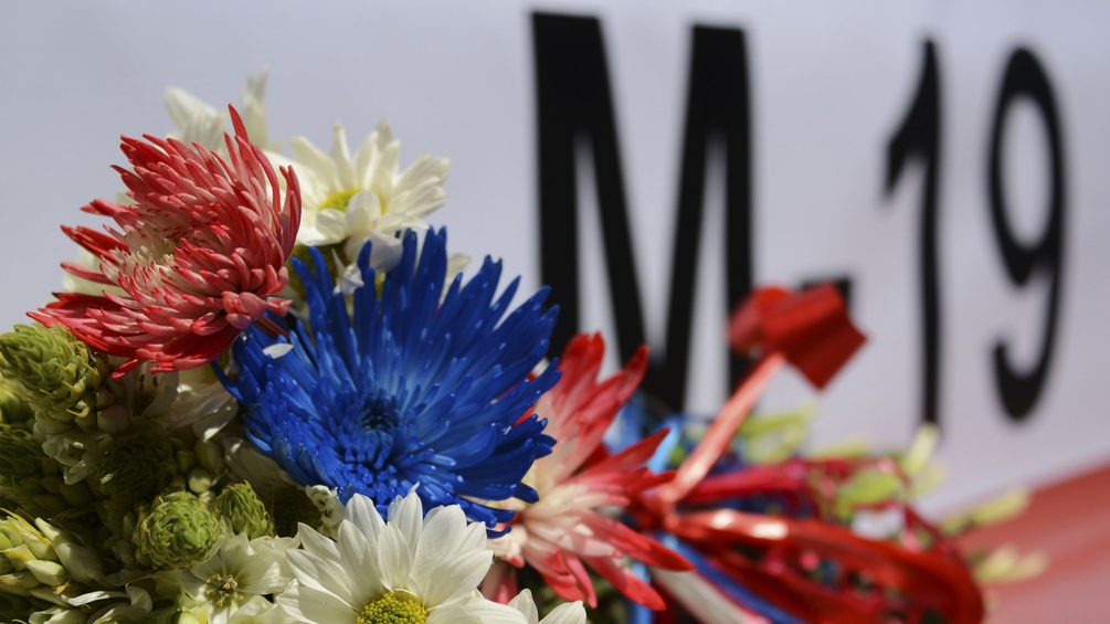 Blumen vor einer Flagge mit M-19 Aufschrift