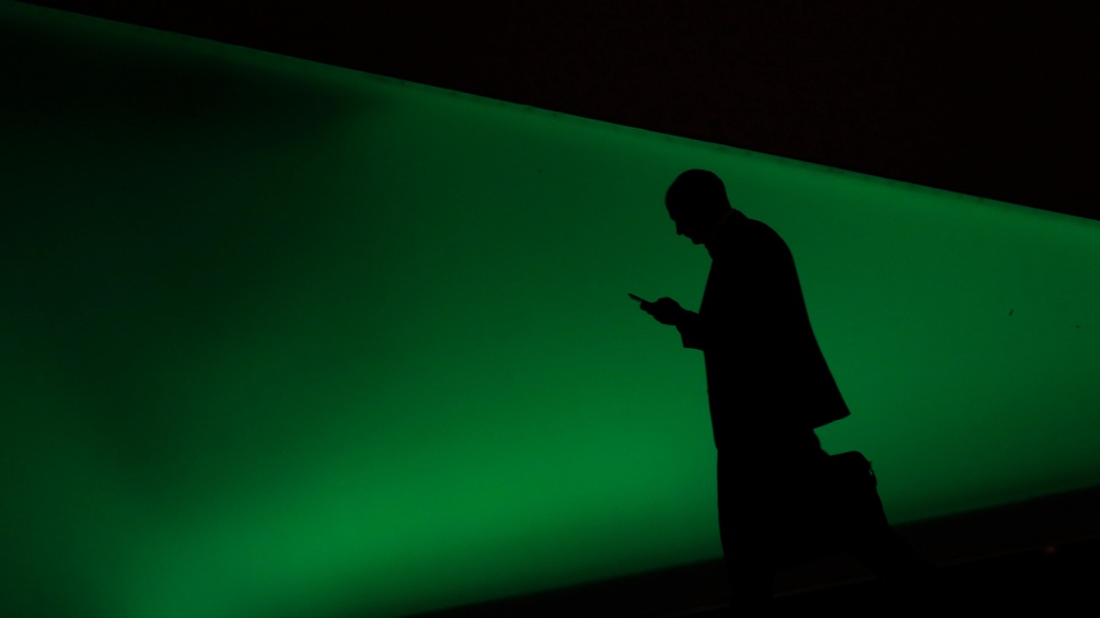 In einem grünen Licht sieht man den Schatten eines Mannes, der auf sein Smartphone starrt.