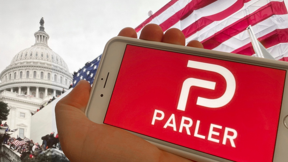 Die App "Parler" auf dem Display eines Handies, dahinter das Capitol