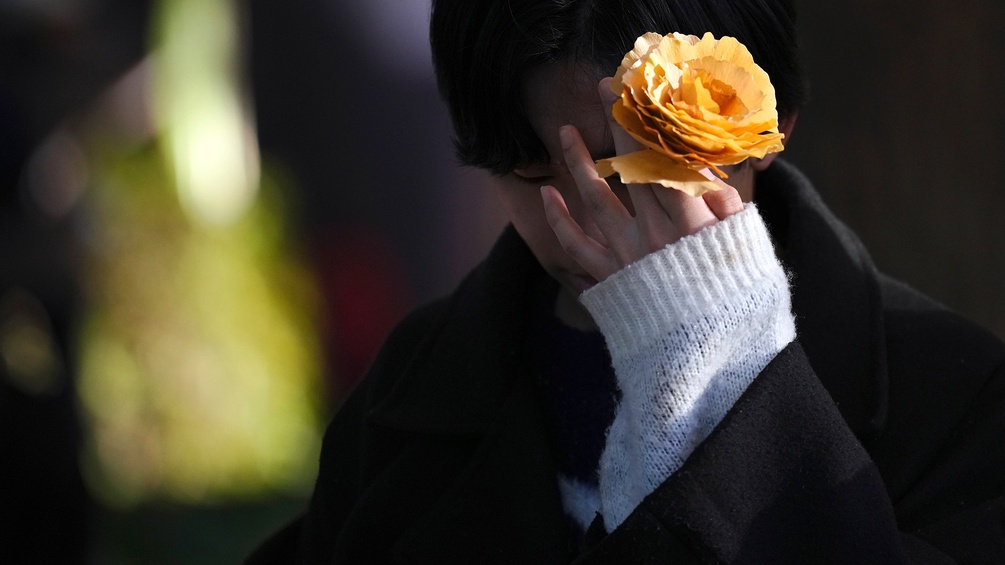 Person in Tokyo mit einer gelben Rose in einer Hand vor dem Gesicht