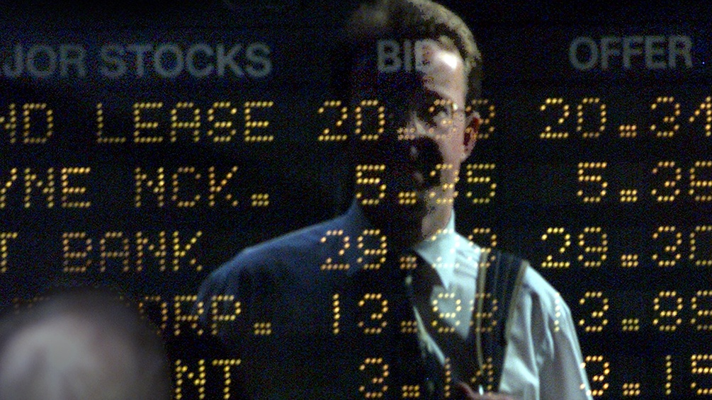 Ein Mann steht vor einem Screen mit Börsenanzeigen